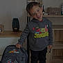 child, smiling, hoodie, spongebob, backpack, cars, lightning_mcqueen, shoes, indoor, mirror, shelf, wooden_furniture, toy, person, happy, standing, casual_clothing, young_boy, black_pants, colorful_clothing