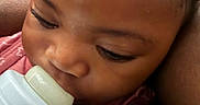 Vanessa is registered to the contest to win money with this photo: baby, bottle, close_up, face, feeding, infant, skin, hand, red_blanket, sleepy, child, mouth, nourishment, comfort, young, portrait, candid, indoors, person, soft_light