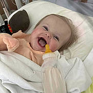 Sawyer is registered to the contest to win money with this photo: baby, smiling, bottle, blanket, crib, toy, infant, happy, face, child, bed, clothing, indoor, cute, person, milk, pale_skin, head, soft_toy, sleeping_area