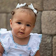 Selina joined the competition — help win amazing prizes! baby, child, girl, white_dress, bows, hair_accessories, portrait, face, cute, curious, outdoor, stone_wall, soft_lighting, closeup, infant, smiling, person, young_child, pretty, fashion