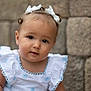 baby, child, girl, white_dress, bows, hair_accessories, portrait, face, cute, curious, outdoor, stone_wall, soft_lighting, closeup, infant, smiling, person, young_child, pretty, fashion