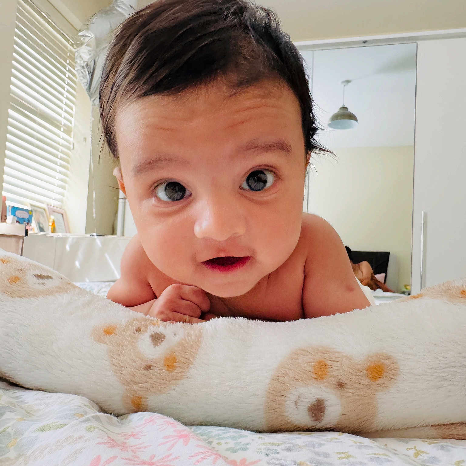 Stethan is registered to the contest to win money with this photo: baby, balloon, bear_pattern, bedroom, blanket, child, cozy, curious, eyes, face, hair, indoors, infant, lamp, lying_down, mirror, person, skin, soft_toy, window_blinds