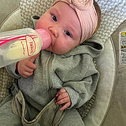 Isabella is registered to the contest to win money with this photo: baby, bottle, headband, clothing, seat, infant, feeding, pink, gray, hand, face, cushion, pattern, indoor, closeup, portrait, cozy, child, sitting, bottle_feeding