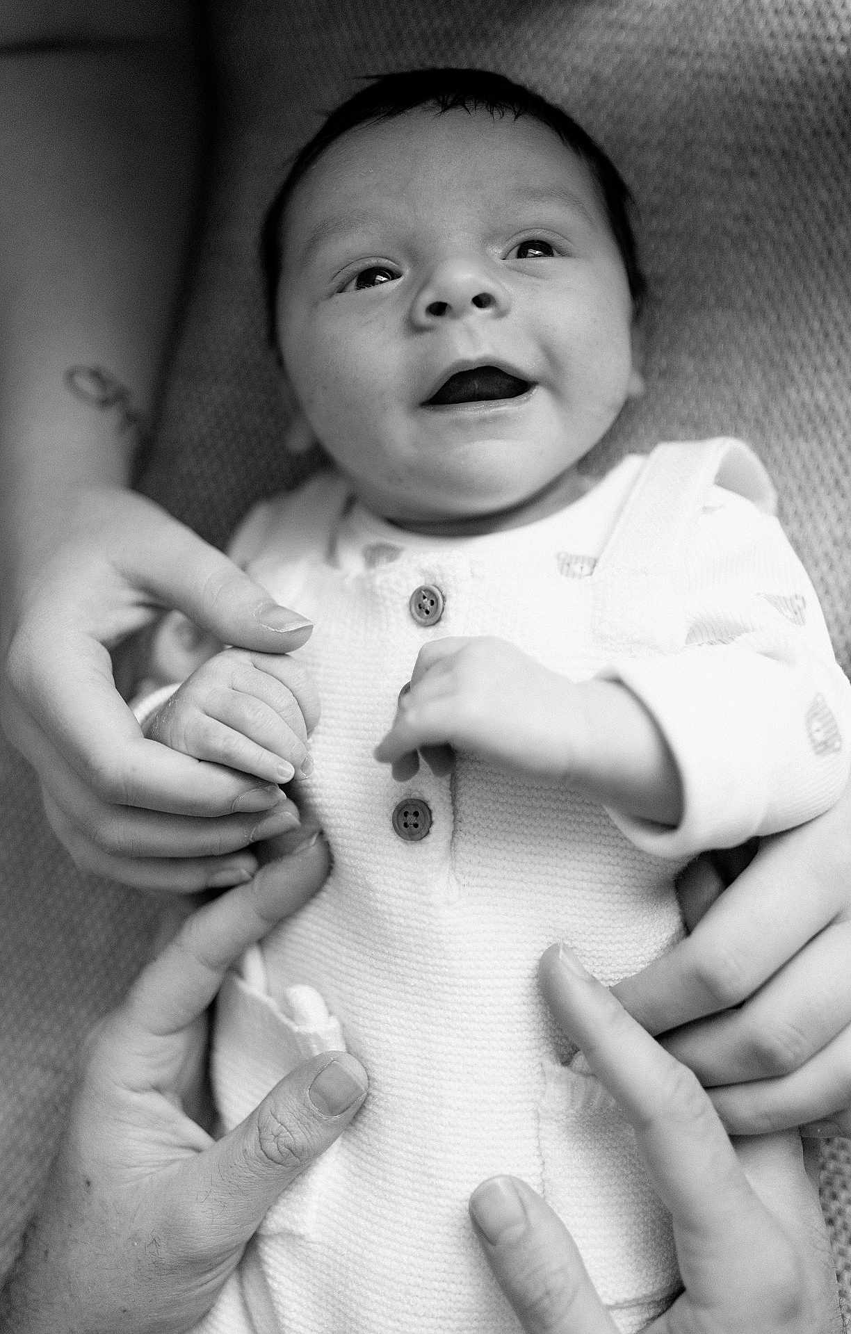 Albie is registered to the contest to win money with this photo: baby, infant, hands, holding, white_clothing, smiling, portrait, black_and_white, closeup, cute, child, person, texture, fabric, button, skin, happy, newborn, family, love
