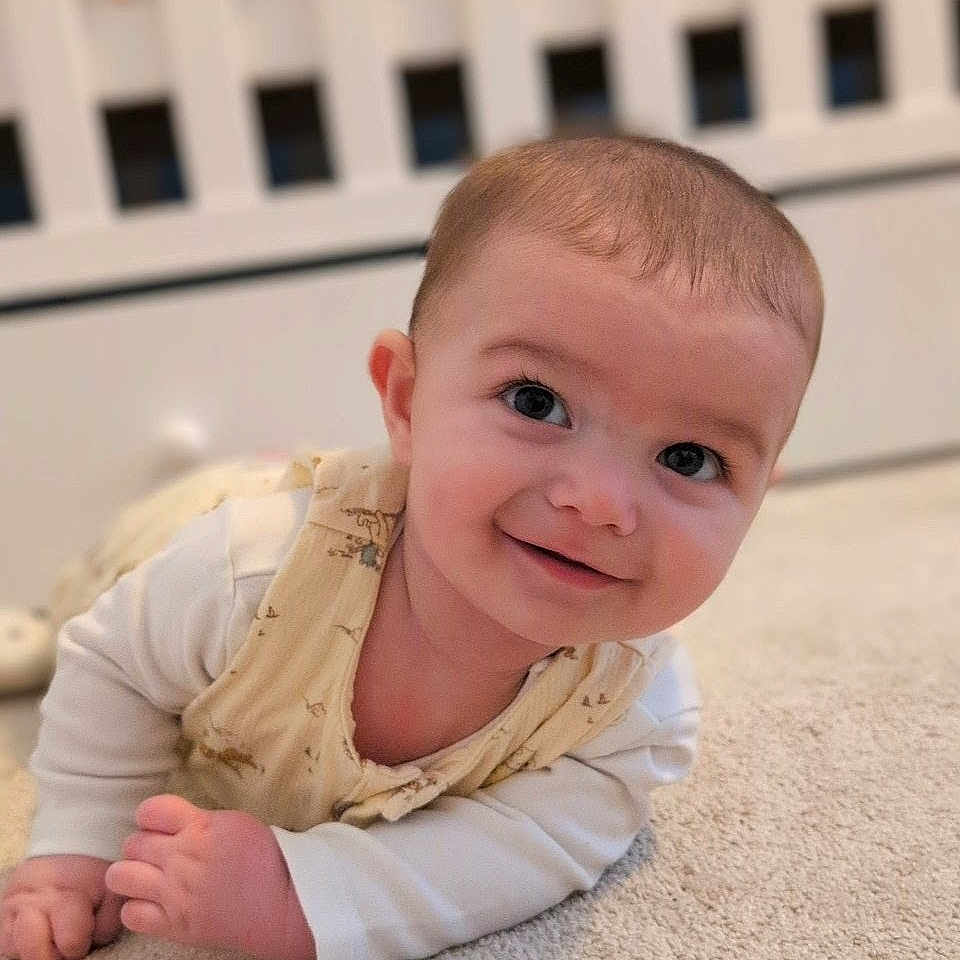 Luca joined the competition — help win amazing prizes! apparel, baby, bedroom, carpet, child, comfort, crawling, crib, cute, expression, eyes, face, hand, indoors, infant, person, skin, sleeve, smiling, young