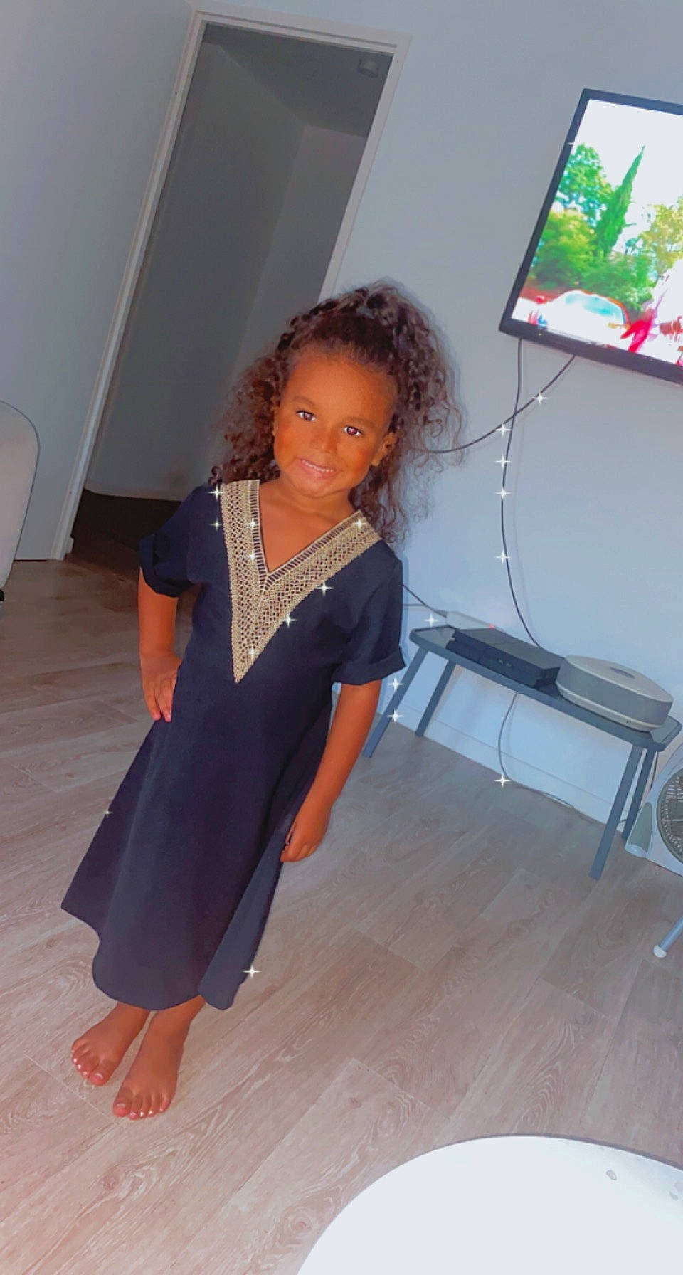 Inaya participe au concours pour gagner de l'argent avec cette photo : day_dress, event, fashion_design, flooring, formal_wear, fun, hair, hardwood, human_leg, joint, joy, knee, long_hair, neck, one_piece_garment, pattern, person, sleeve, television, trunk