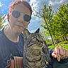Chaoz participe au concours pour gagner de l'argent avec cette photo : person, cat, tabby_cat, outdoor, trees, greenery, sky, clouds, sunlight, sunglasses, red_hair, bag, hand, tattoo, animal, pet, nature, leash, casual, portrait