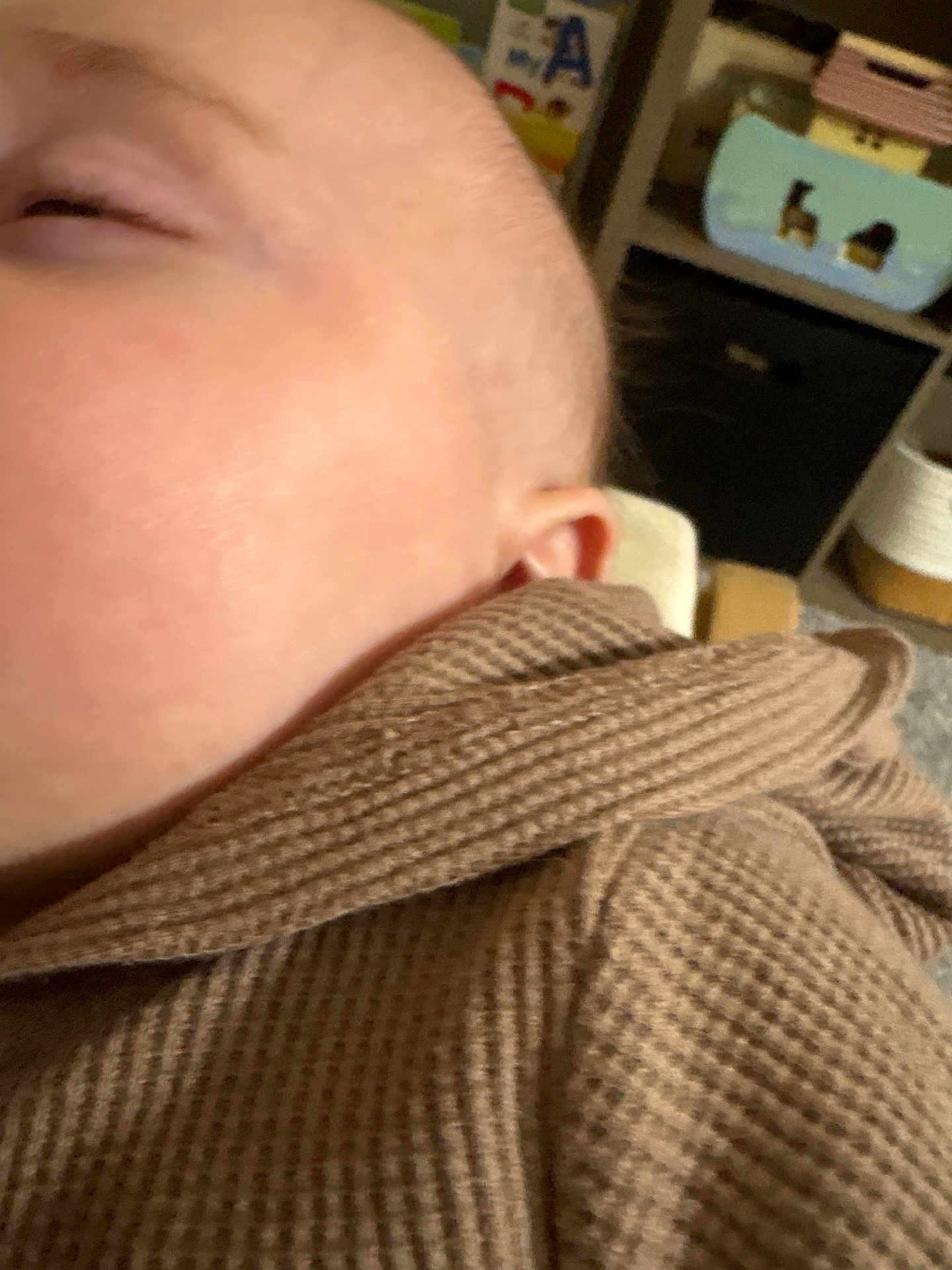 Kasen is registered to the contest to win money with this photo: baby, infant, close_up, cheek, ear, eyelid, skin, blurry, brown_cloth, waffle_texture, cozy, sleeping, nursery, toy, shelf, indoor, portrait, soft_fabric, face, handheld_photo