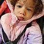 child, toddler, face, blue_eyes, curly_hair, pink_jacket, hood, car_seat, harness, close_up, winter_clothing, coat, portrait, young_child, baby, seatbelt, expression, indoor, cute, warm_clothes