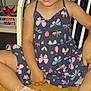 butterfly_pattern, calm_expression, casual_clothing, chair, child, colorful, curly_hair, cute, dress, feet, footwear, furniture, indoor, looking_at_camera, person, pink_shoes, portrait, sitting, wooden_floor, young