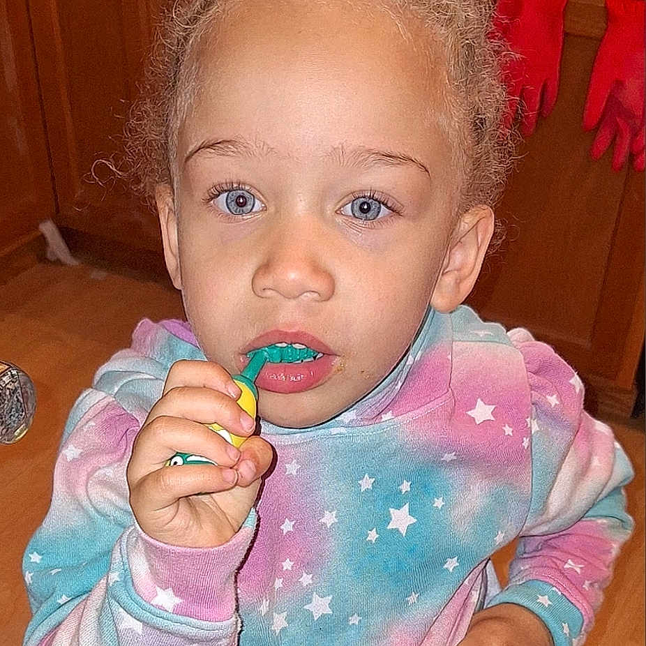 Denali joined the competition — help win amazing prizes! blue_eyes, casual, child, curly_hair, expression, face, floor, hand, indoor, kitchen, mouth, pastel_clothing, person, portrait, red_gloves, star_pattern, sweatshirt, toothbrush, wooden_cabinets, young_child