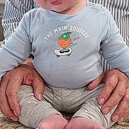 Roan joined the competition — help win amazing prizes! baby, child, infant, person, face, tongue, blue_eyes, curly_hair, shirt, cartoon, text_on_clothing, hands, kitchen_counter, marble_surface, sitting, playful, cute, adult_hands, casual_clothing, indoor