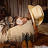 baby, sleeping, blanket, knitted, wooden_bed, cowboy_hat, cowboy_boots, rustic, cozy, nursery, brown, beige, plaid_clothing, soft_lighting, indoor, decor, western_theme, infant, peaceful, cute