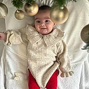 Mya a rejoint le concours — aidez-le/la à gagner de superbes lots ! baby, infant, smile, knitted_sweater, red_leggings, reindeer_pattern, blanket, christmas_tree, golden_baubles, festive, holiday, cute, indoors, child, portrait, happy, cozy, winter_clothing, celebration, face