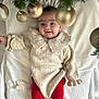 baby, infant, smile, knitted_sweater, red_leggings, reindeer_pattern, blanket, christmas_tree, golden_baubles, festive, holiday, cute, indoors, child, portrait, happy, cozy, winter_clothing, celebration, face