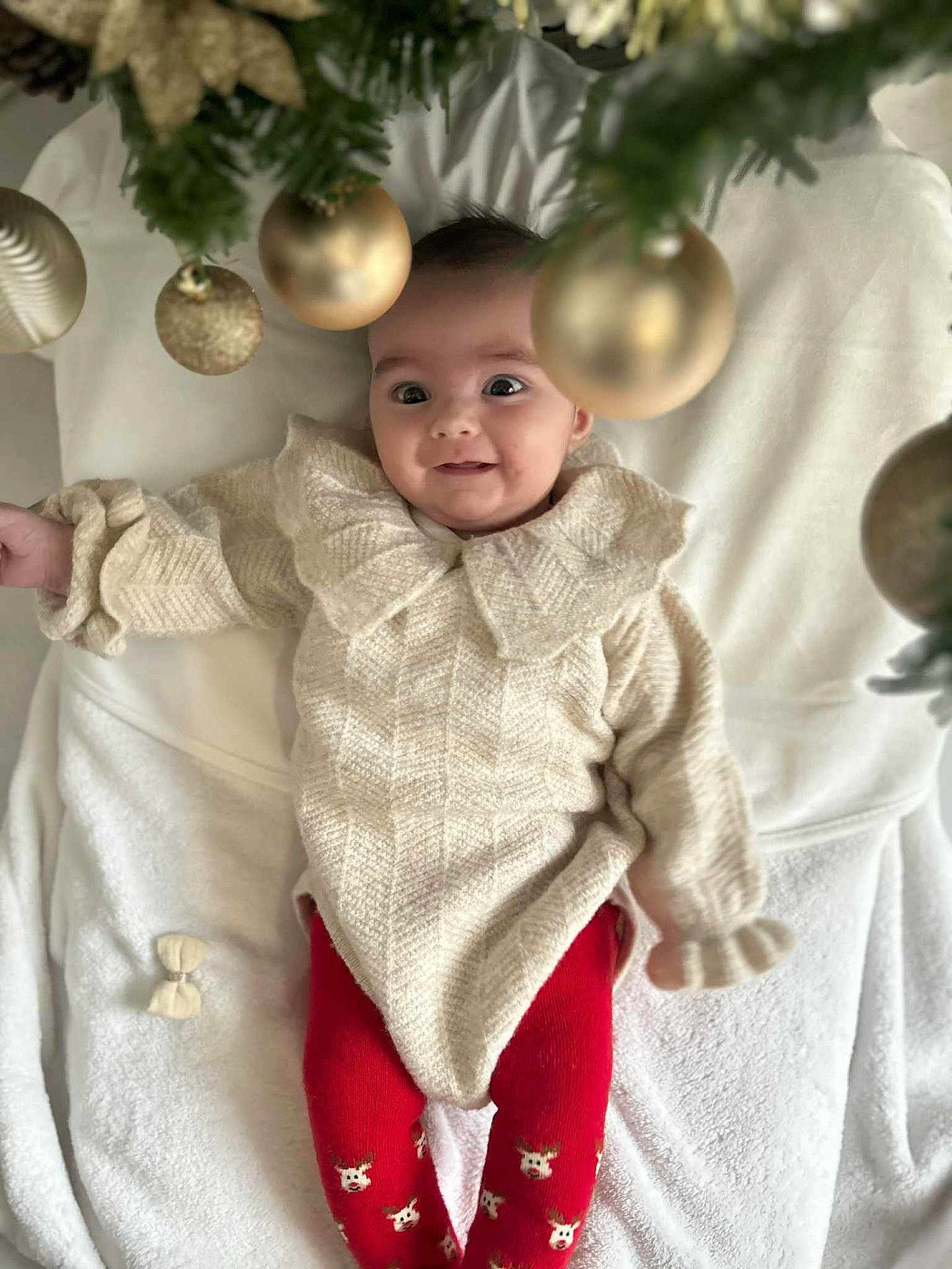 Mya a rejoint le concours — aidez-le/la à gagner de superbes lots ! baby, infant, smile, knitted_sweater, red_leggings, reindeer_pattern, blanket, christmas_tree, golden_baubles, festive, holiday, cute, indoors, child, portrait, happy, cozy, winter_clothing, celebration, face