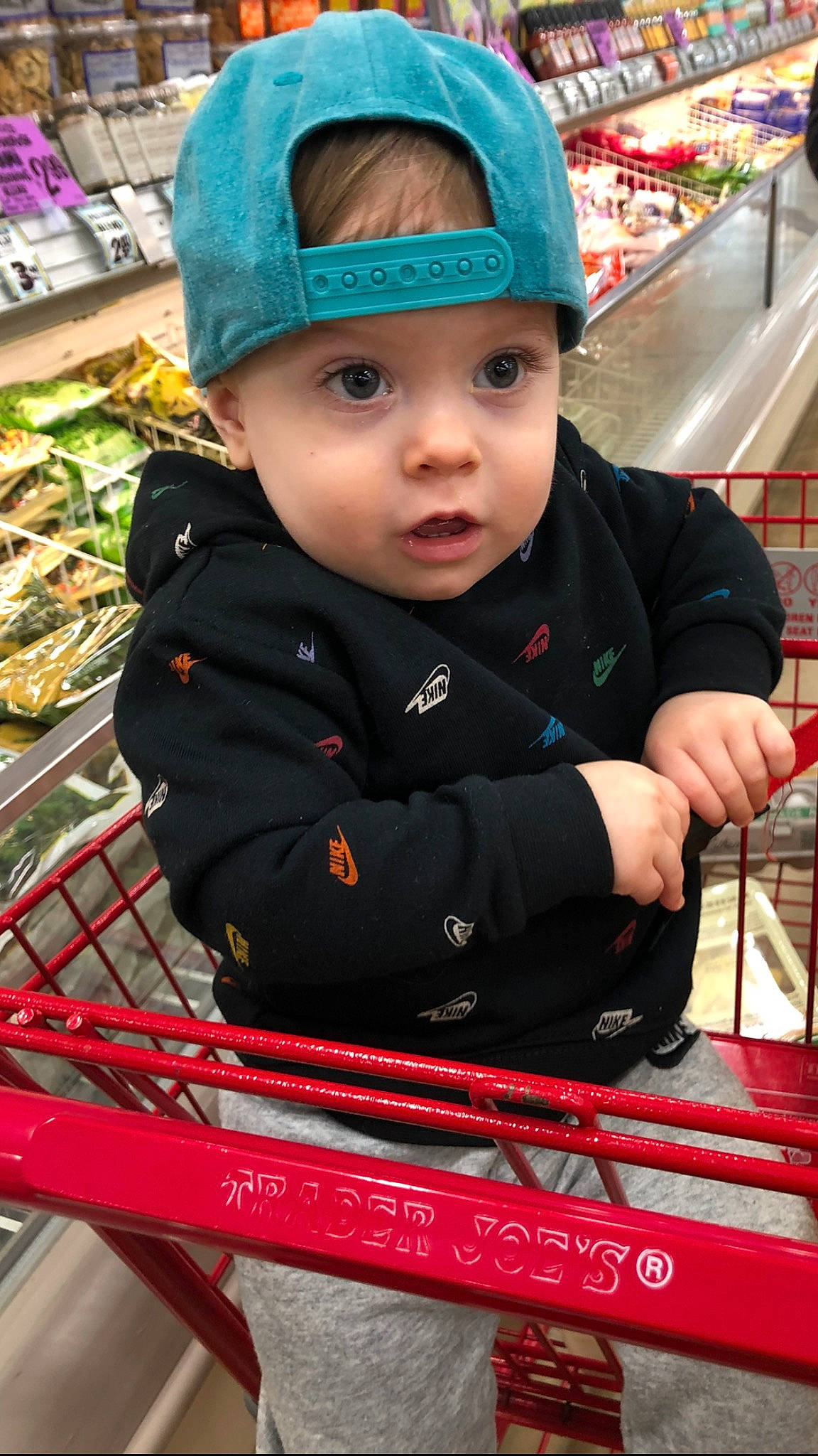 John is registered to the contest to win money with this photo: baby, baby_toddler_clothing, basket, cap, carmine, child, city, customer, electric_blue, fashion_accessory, fun, headwear, person, retail, service, shopping_cart, sitting, sleeve, toddler