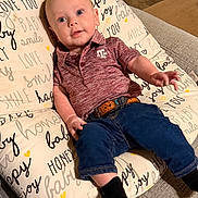 Cooper is registered to the contest to win money with this photo: baby, infant, child, polo_shirt, jeans, socks, cushion, couch, indoor, smile, curious, face, person, clothing, text, home, comfortable, seated, reaching, casual