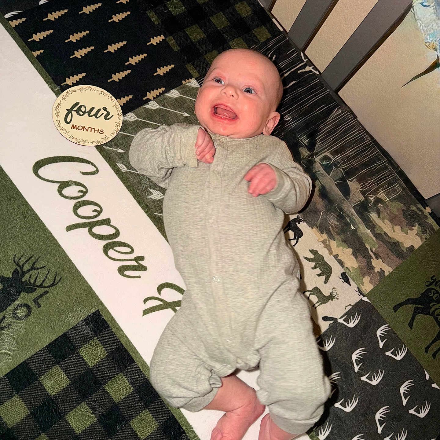 Cooper joined the competition — help win amazing prizes! baby, infant, crib, blanket, onesie, smiling, face, child, pattern, animal_print, plaid, milestone, four_months, happy, lying_down, cozy, indoor, person, cute, home