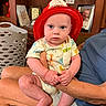Cooper is registered to the contest to win money with this photo: baby, child, infant, firefighter_hat, red_hat, animal_print_clothing, onesie, sitting, arms, legs, person, indoor, furniture, laundry_basket, framed_photo, wooden_shelf, skin, cute, expression, adult_arm