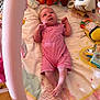 baby, infant, striped_clothing, plush_toy, play_mat, colorful, pink, soft_toys, infant_garment, baby_accessories, floor, wooden_floor, toy, child, lying_down, cute, indoors, small_person, looking_up, raised_arms