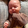 baby, sleeping, blanket, brown_clothing, bear_design, pillow, cozy, infant, soft_texture, indoor, child, peaceful, cute, resting, face, hand, closed_eyes, plush, comfort, nap