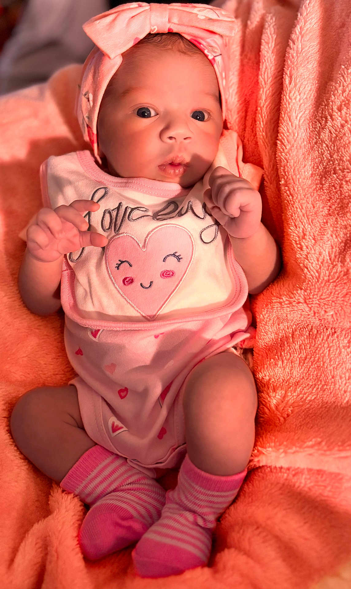 Amiyah is registered to the contest to win money with this photo: baby, infant, pink_clothing, headband, socks, blanket, soft_texture, cute, portrait, indoor, newborn, face, hands, lying_down, cozy, baby_girl, expression, closeup, warm_colors, sleepwear