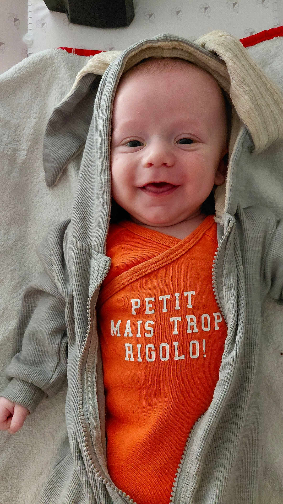 Lenny participe au concours pour gagner de l'argent avec cette photo : baby, smiling, hoodie, orange_shirt, text, blanket, infant, cute, child, happy, face, apparel, clothing, portrait, indoor, baby_garment, soft_texture, young_child, casual_wear, relaxed