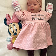 élïna a rejoint le concours — aidez-le/la à gagner de superbes lots ! adorable, baby, blanket, cartoon, child, cozy, cute, footwear, headwrap, indoors, infant, lying_down, minnie_mouse, mittens, pink_dress, resting, sleeping, soft_toys, text_on_clothing, young_child