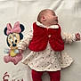 élïna a rejoint le concours — aidez-le/la à gagner de superbes lots ! baby, blanket, cartoon_character, child, cozy, cute, fabric, footwear, indoors, infant, minnie_mouse, name_text, patterned_clothing, portrait, red_vest, resting, sleeping, soft_texture, white_dress, young
