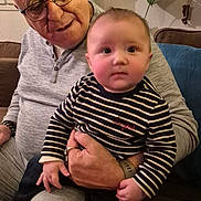 Temae a rejoint le concours — aidez-le/la à gagner de superbes lots ! elderly_man, baby, child, striped_shirt, glasses, couch, indoor, plants, home_decor, cozy, family, holding, socks, portrait, seated, casual_clothing, living_room, affection, tender_moment, people