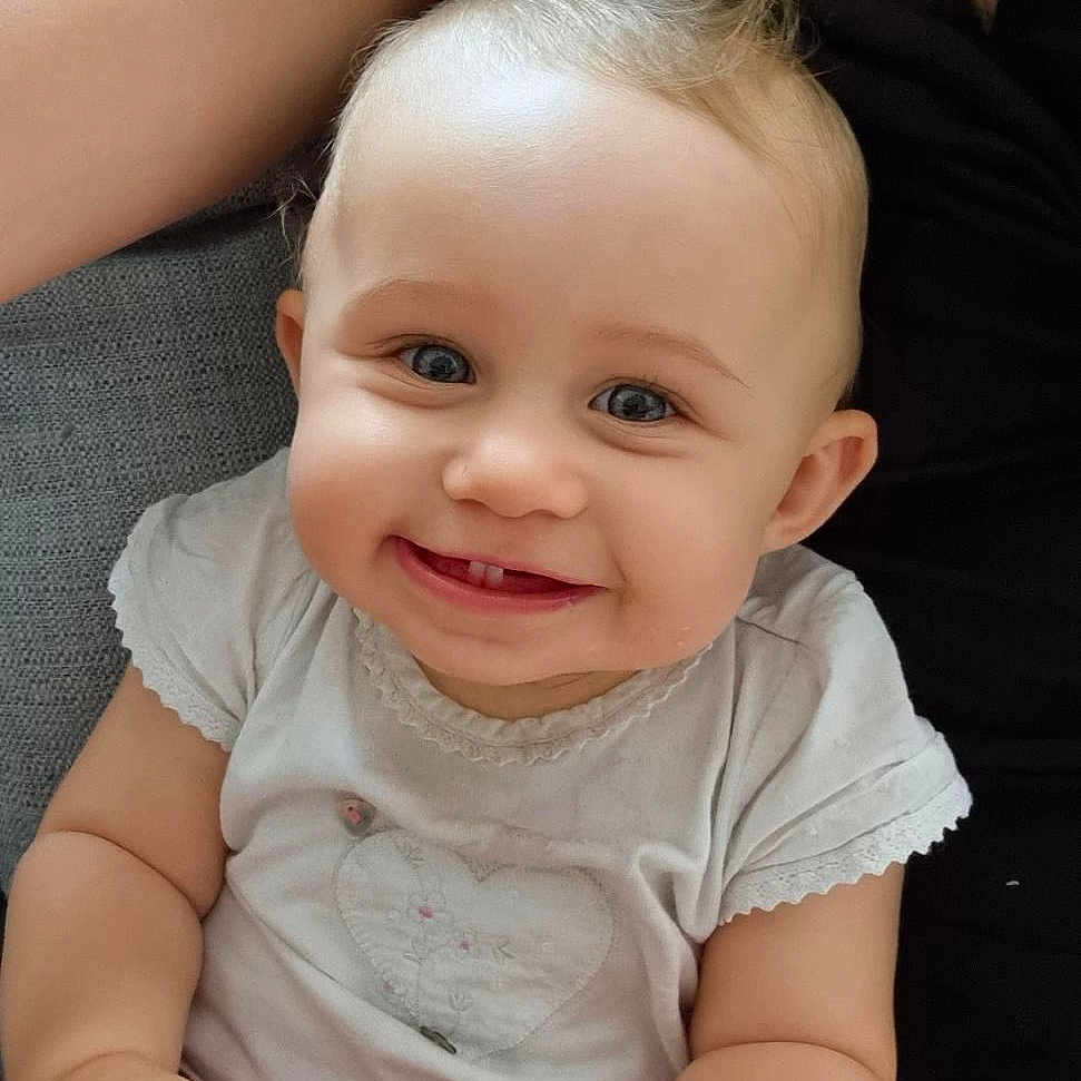 Mia participe au concours pour gagner de l'argent avec cette photo : arm, baby, blue_eyes, child, closeup, couch, cute, happy, heart_design, human, indoor, infant, person, portrait, seated, short_sleeves, skin, smiling, toothy_grin, white_shirt