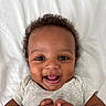 baby, smiling, happy, infant, face, cute, child, closeup, portrait, hands, clothing, curly_hair, lying_down, light_grey_shirt, white_background, skin, young_child, joyful, playful, expressive