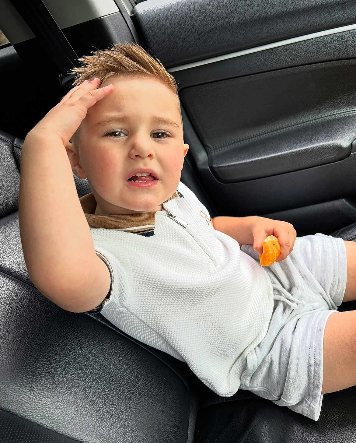 Nicolas joined the competition — help win amazing prizes! child, boy, car, car_seat, orange, fruit, shorts, white_shirt, hand, hair, expression, leather, interior, seatbelt, casual_clothing, portrait, young, candid, sitting, food