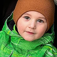 Nicolas is registered to the contest to win money with this photo: beanie, brown_hat, cheeks, child, closeup, cute, eyebrows, eyes, face, green_jacket, hood, outfit, portrait, seat, smile, stroller, toddler, warm_clothing, winter, winter_jacket