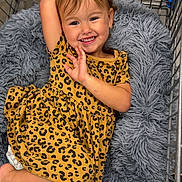 Khelani is registered to the contest to win money with this photo: child, toddler, smile, leopard_print, dress, shopping_cart, cushion, plush, happy, cute, person, clothing, indoors, relaxing, comfort, young_child, portrait, skin, face, hair