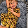 child, toddler, smile, leopard_print, dress, shopping_cart, cushion, plush, happy, cute, person, clothing, indoors, relaxing, comfort, young_child, portrait, skin, face, hair