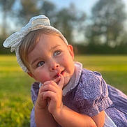 Khelani is registered to the contest to win money with this photo: toddler, child, girl, headband, bow, purple_dress, outdoor, grass, sunlight, portrait, cute, thinking, daylight, nature, baby, face, hands, smile, young, person