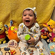 Ezekiel is registered to the contest to win money with this photo: baby, child, smiling, sitting, plush_toys, winnie_the_pooh, tiger, piglet, clothing, headband, yellow_background, toy_bottle, 9_months, happy, cute, indoors, celebration, colorful, cartoon, portrait