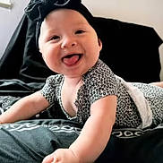 Sequoia joined the competition — help win amazing prizes! baby, smiling, tongue_out, headband, black_bow, lying_down, bed, blanket, patterned_clothing, infant, happy, cute, young_child, indoor, person, portrait, skin, face, hand, crawling_position