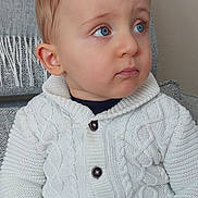 Noah participe au concours pour gagner de l'argent avec cette photo : child, toddler, baby, face, blue_eyes, sweater, knit_cardigan, buttons, ear, hands, portrait, indoor, couch, blanket, looking_away, expression, skin, red_pants, seat, cozy