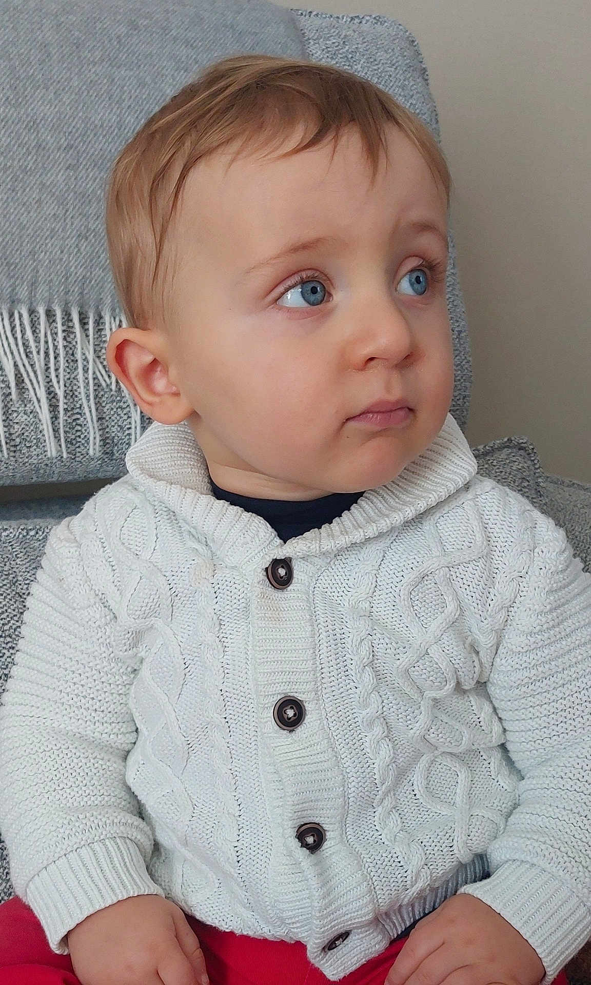 Noah participe au concours pour gagner de l'argent avec cette photo : child, toddler, baby, face, blue_eyes, sweater, knit_cardigan, buttons, ear, hands, portrait, indoor, couch, blanket, looking_away, expression, skin, red_pants, seat, cozy