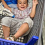 child, shopping_cart, smiling, striped_pants, plaid_shirt, blue_plastic, store_aisle, tiled_floor, footwear, happy, person, indoor, retail, casual_clothing, young_child, hands_up, blue_bag, metal_frame, grid_pattern, relaxed