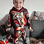 child, boy, tiger_outfit, hoodie, pants, socks, couch, toy_fire_truck, toy, living_room, blanket, pillow, face, expression, playful, indoor, person, home, smile, fun