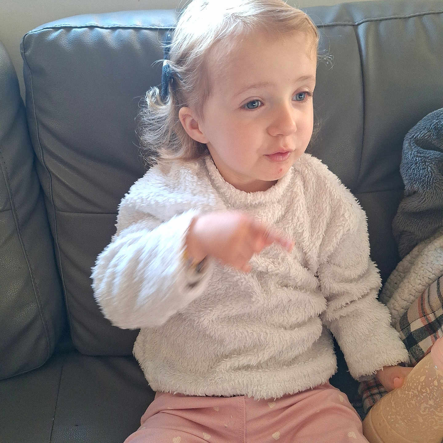 Bélyne participe au concours pour gagner de l'argent avec cette photo : bottle, casual_clothing, child, couch, cozy, drink, expression, hair_clip, heart_pattern, indoor, leather, natural_light, person, pink_pants, pointing, seated, sweater, toddler, window, young_child