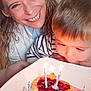 woman, child, birthday, cake, candles, celebration, dessert, food, plate, happy, smiling, curly_hair, striped_shirt, indoor, table, closeup, family, home, light, face