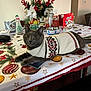 cat, sweater, table, holiday, tablecloth, flower_arrangement, holiday_decor, snacks, dog_bowl, indoor, gray_cat, festive, centerpiece, fruit, vase, decorations, relaxed, pet, cozy, christmas