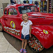 Roselynn is registered to the contest to win money with this photo: child, smiling, red_car, plush_toys, store_interior, tiled_floor, tshirts, mannequins, display_shelves, casual_clothing, purple_sandals, vintage_car, bright_lighting, retail_store, happy_child, indoor, colorful, young_person, shopping, person