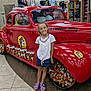 child, smiling, red_car, plush_toys, store_interior, tiled_floor, tshirts, mannequins, display_shelves, casual_clothing, purple_sandals, vintage_car, bright_lighting, retail_store, happy_child, indoor, colorful, young_person, shopping, person