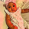 Verity Reign is registered to the contest to win money with this photo: baby, child, infant, portrait, lying_down, pink_bow, headband, floral_outfit, romper, bed, blanket, fluffy_blanket, indoors, face, eyes, serious_expression, warm_lighting, colorful_lighting, closeup, photography